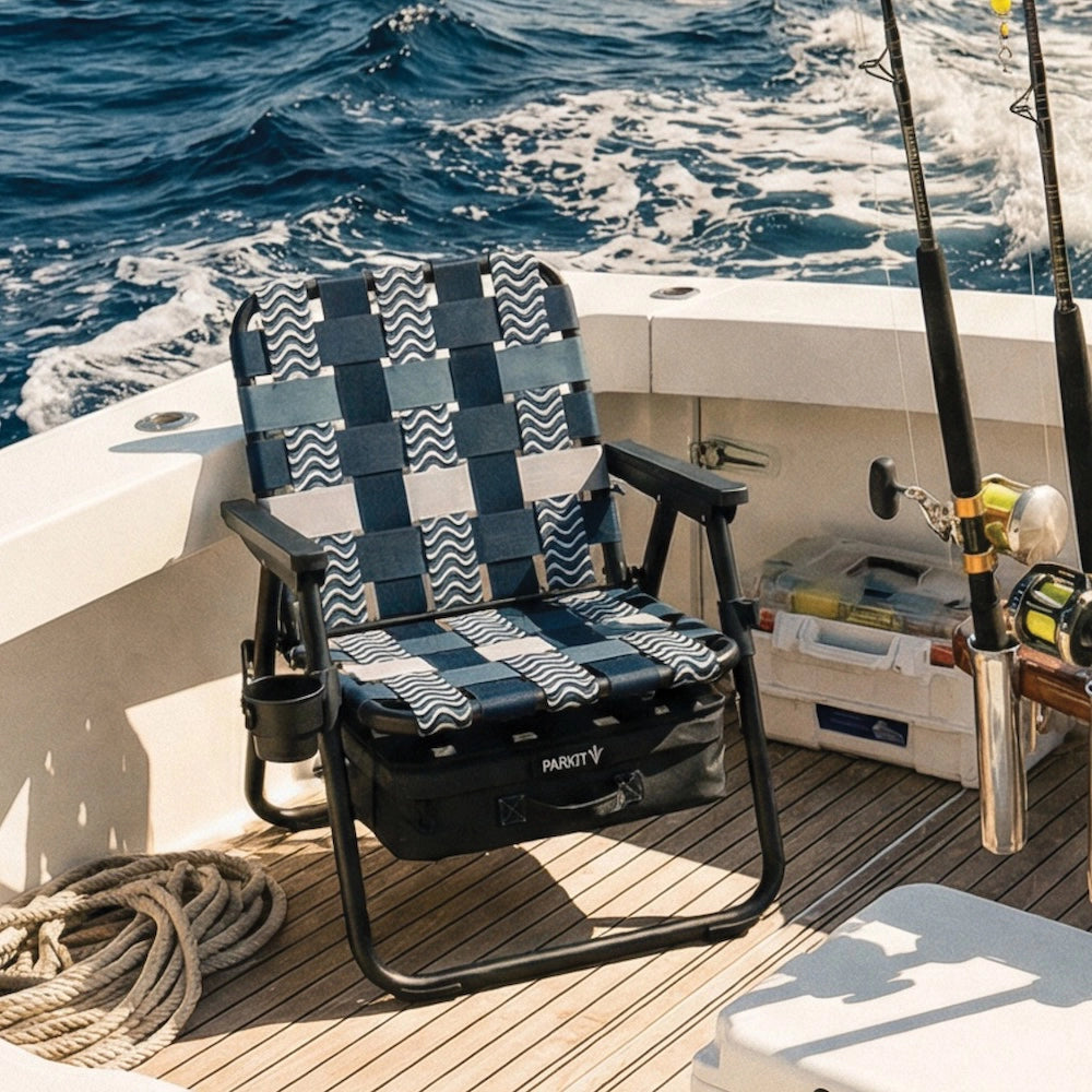 PARKIT Voyager Outdoor Chair with Cooler, featuring a blue and white wavy pattern, on a boat deck with fishing rods.